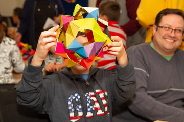 A child shows off their colourful origami creation